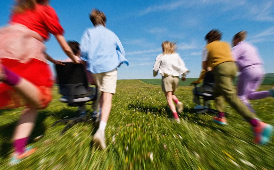 Een groep mensen rent met bureaustoelen door een weiland